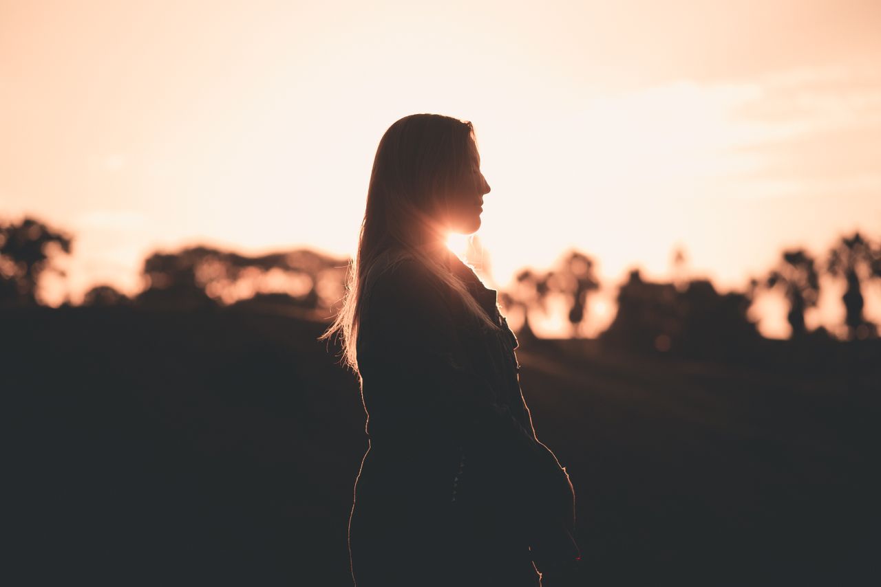 A serene silhouette of a woman during sunset with a warm glow and nature backdrop.